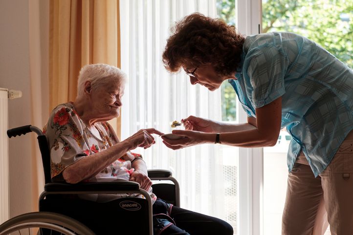 Eine Frau hilft einer alten Frau Seniorin im Rollstuhl beim Essen