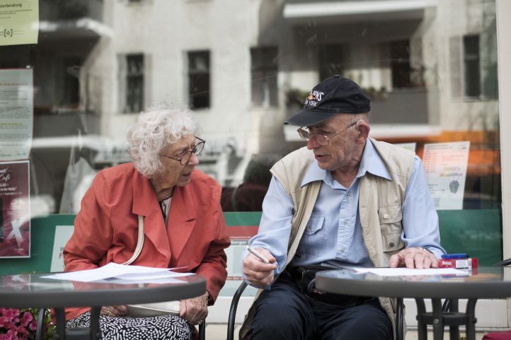 Zwei Senioren sitzen draußen in einem Café. 
