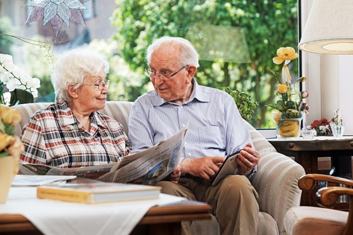 Älteres Paar sitzt auf dem Sofa mit Tablet-Computer und Zeitung.