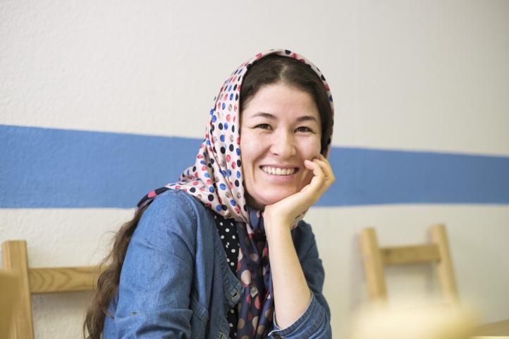 Eine Frau mit Kopftuch stützt das Kinn in die Hand und lächelt dabei
