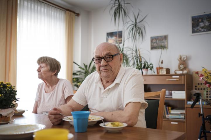 Älterer Mann mit Brille und ältere Frau in einer Pflegeeinrichtung sitzen am Tisch und essen