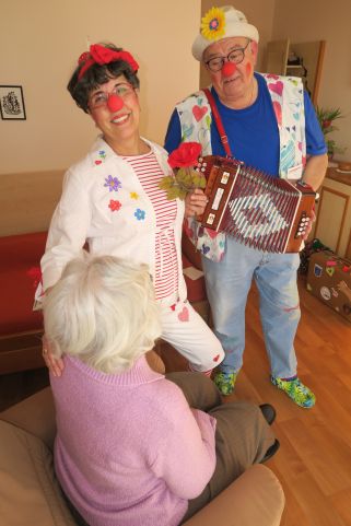 Zwei ehrenamtliche Pflegeclowns spielen Akkordeon für eine Seniorin