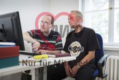 Zwei Männer sitzen am PC, während der eine tippt und beide auf den Monitor blicken