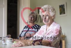 Zwei ältere Damen sitzen an einem Tisch und lächeln in die Kamera