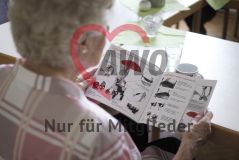 Aufnahme über die Schulter einer älteren Frau hinweg, die gerade in einem Katalog zur Rollatoren blättert