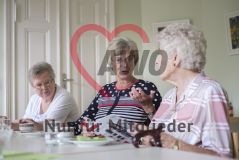 Drei ältere Damen sitzen an einem Tisch, blättern in einem Katalog und unterhalten sich über Rollatoren
