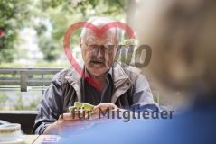 Ein älterer Mann sitzt im Freien an einem Tisch, spielt Karten und blickt auf sein Blatt