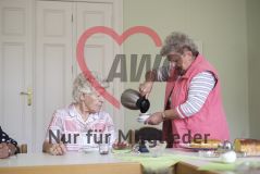 Eine ältere Frau sitzt am Tisch und sieht dabei zu, wie eine andere Frau ihr stehend Kaffee einschenkt
