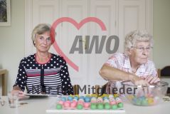 Zwei ältere Frauen sitzen am Tisch vor einem Spielfeld mit bunten Kugeln und spielen Bingo