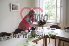 Eine ältere Frau schmückt einen eingedeckten Tisch und stellt Blumen in eine Vase