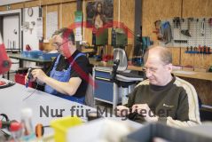 Zwei Männer sitzen in einer Werkstatt und arbeiten mit Kabeln