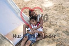 zwei Kinder umarmen sich auf dem Spielplatz und lachen in die Kamera