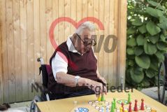 Ein alter Mann Senior im Rollstuhl sitzt draußen und spielt ein Brettspiel