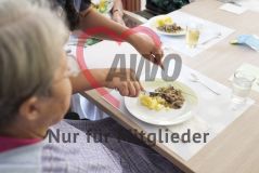 Eine Frau hilft einer alten Frau Seniorin beim Essen neben weiteren Seniorinnen und Senioren