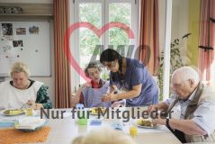Eine Frau hilft einer alten Frau Seniorin beim Essen neben weiteren Seniorinnen und Senioren in einer Einrichtung