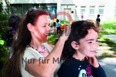 Eine Frau bindet einem Kind Mädchen die Haare auf einem Spielplatz