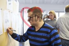 Ein junger Mann nimmt an einem Workshop Seminar teil und schreibt mit einem Stift auf ein Blatt an einer Pinnwand