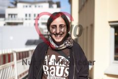 Eine junge Frau mit T-Schirt Nazis raus aus den Stadien mit Piercing steht draußen und lächelt in die Kamera