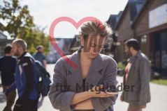 Eine junge Frau steht draußen und tippt auf dem Handy Smartphone und mehrere Menschen im Hintergrund