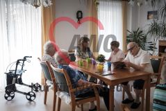 Ältere Bewohner*innen einer Pflegeeinrichtung sitzen um einen Tisch im Hintergrund ein Rollator