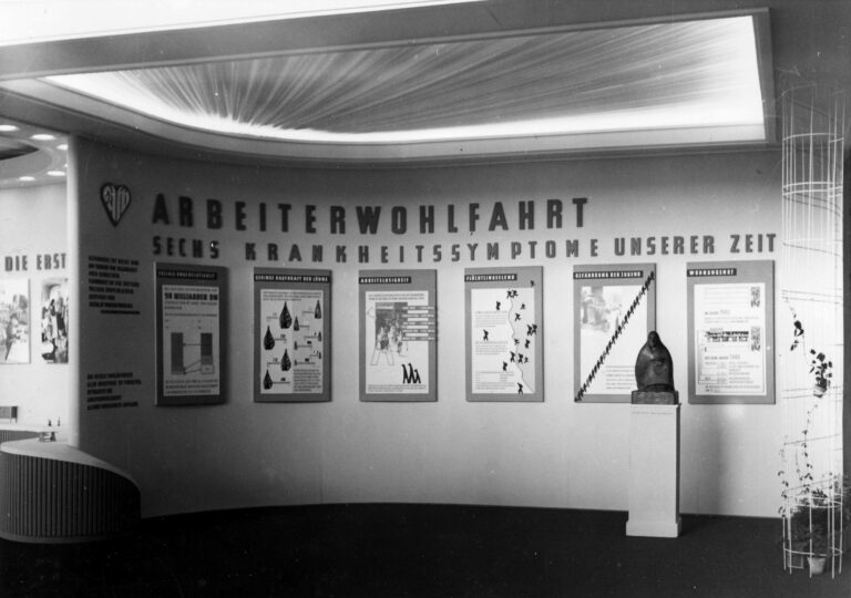 Schwarz-Weiß-Fotografie einer Ausstellung der Arbeiterwohlfahrt (AWO) mit dem Titel "Sechs Krankheitssymptome unserer Zeit".
