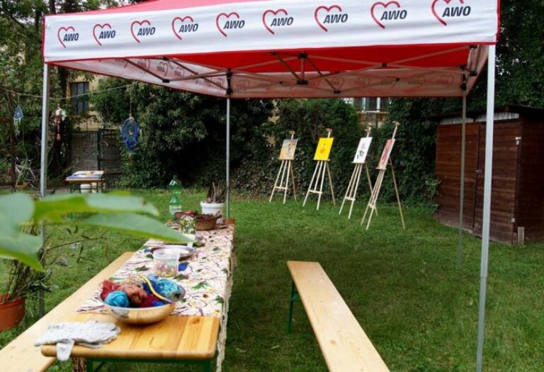 Ein Pavillon mit AWO-Logos steht in einem Garten. Unter dem Pavillon befindet sich ein langer Tisch auf dem verschiedene Bastelmaterialien und Werkzeuge liegen.