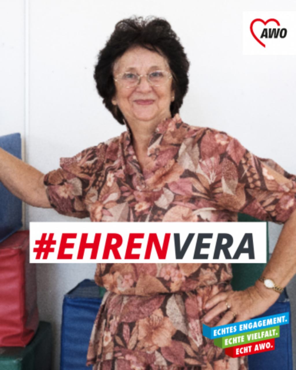 Eine ältere Frau mit dunklem, gelocktem Haar und Brille steht lächelnd vor bunten Schaumstoffblöcken. Sie trägt ein gemustertes Kleid in warmen Farben. In der oberen rechten Ecke ist das Logo der AWO zu sehen. Über ihrem Oberkörper steht der Hashtag "#EHRENVERA" in rot und schwarz. Unten rechts im Bild befindet sich ein farbiger Banner mit der Aufschrift "ECHTES ENGAGEMENT. ECHTE VIELFALT. ECHT AWO."