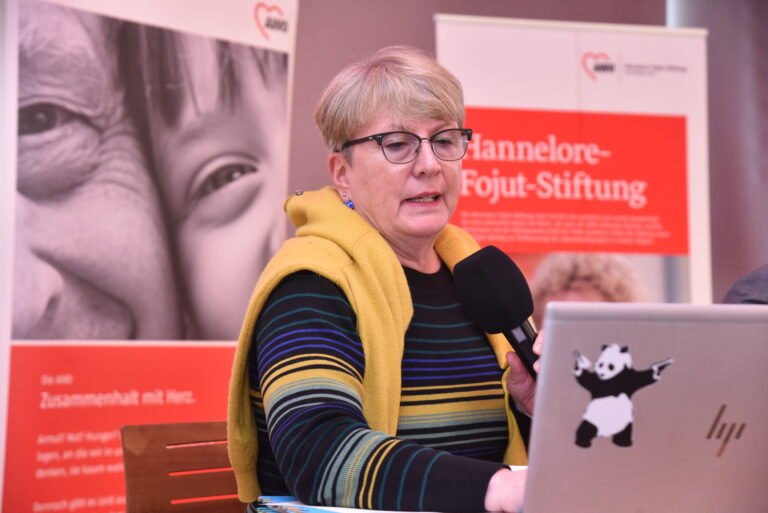 Frau spricht in ein Mikrofon mit AWO-Banner im Hintergrund