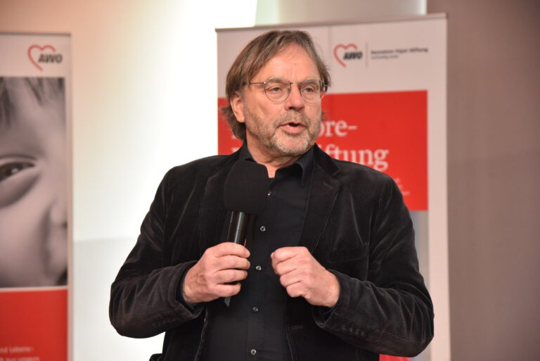 Mann spricht in ein Mikrofon mit einem AWO Banner im Hintergrund