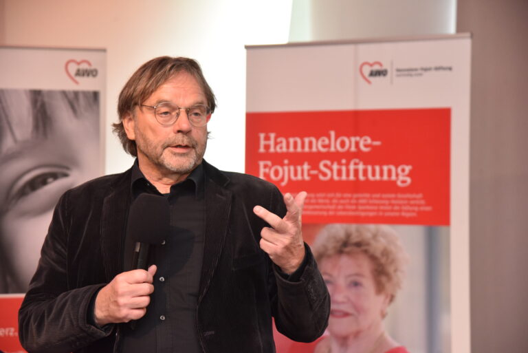 Mann spricht in ein Mikrofon mit einem AWO Banner im Hintergrund