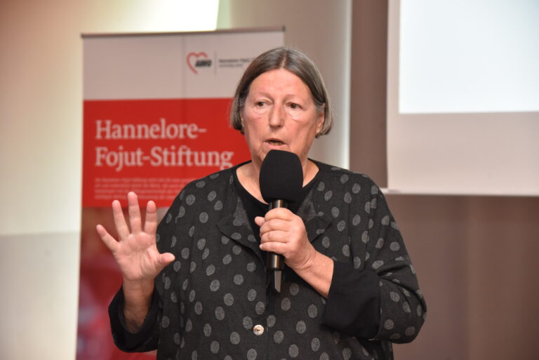 Frau spricht in ein Mikrofon mit einem AWO Banner im Hintergrund