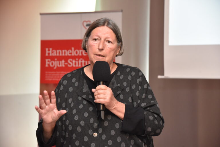 Frau spricht in ein Mikrofon mit einem AWO Banner im Hintergrund