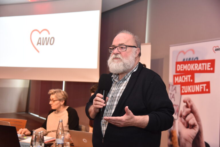 Ein mann spricht in ein Mikrofon mit AWO-Bannern im Hintergrund