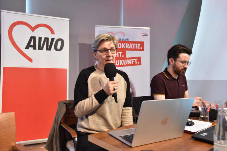 Frau spricht in ein Mikrofon mit AWO-Bannern im Hintergrund