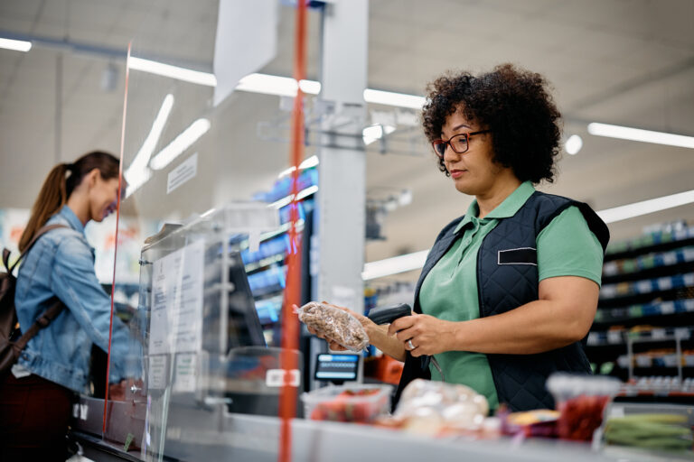 Eine Kassiererin an der Kasse eines Supermarkts, dahinter eine Kundin