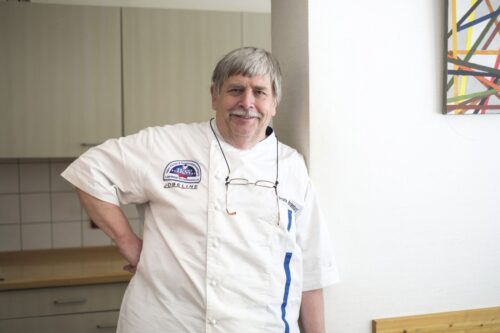 Portrait eines Kochs, der in die Kamera lächelt.