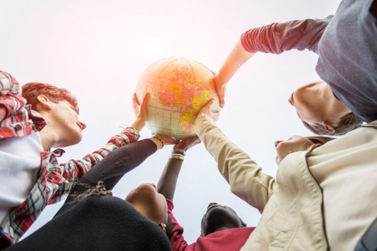 Eine Gruppe von diversen Jugendlichen hält gemeinsam einen Globus in die Luft.