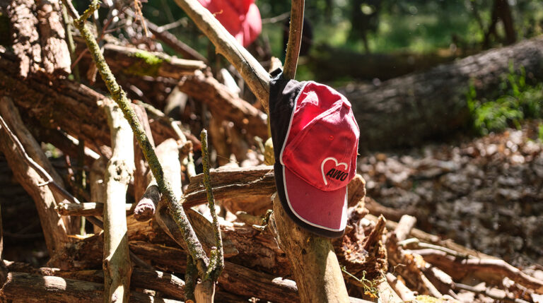 Ein rotes Käppi mit AWO-Logo hängt im Wald an einem Ast.