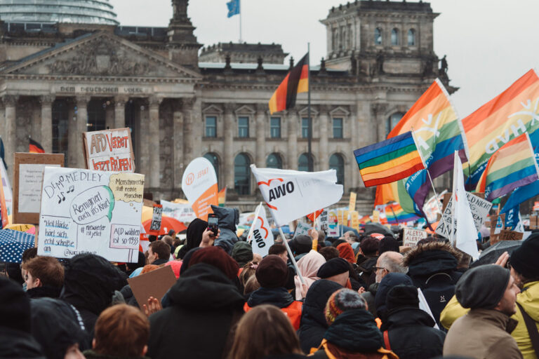 Teilnehmende einer Demonstration vor dem Reichstagsgebäude in Berlin, u.a. mit AWO- und Regenbogen-Flaggen