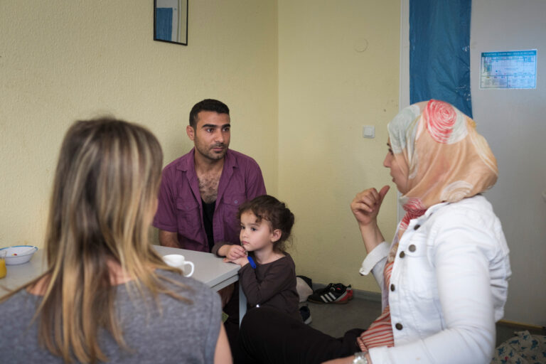 Zwei Frauen, ein Mann und ein kleines Mädchen sitzen an einem Tisch in einer Flüchtlingsunterkunft.