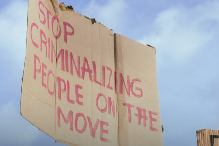 Schild mit der Aufschrift "Stop criminalizing people on the move"