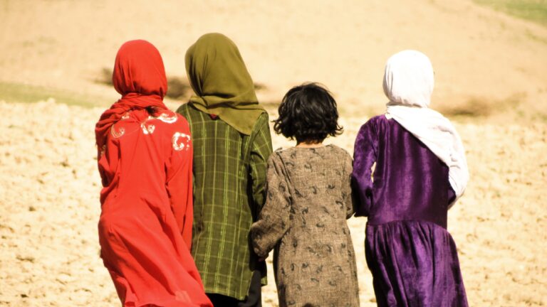Rückenansicht von vier afghanischen Mädchen in bunten Kleidern, drei mit Kopftuch