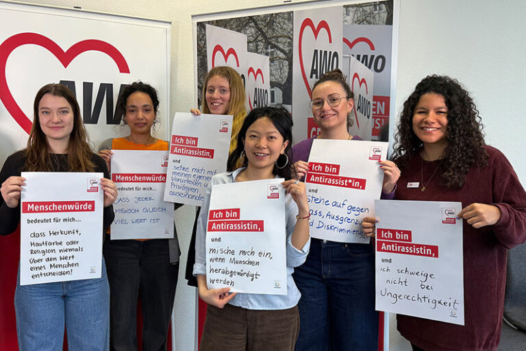 Sechs Frauen halten AWO-Plakaten zu Menschenwürde und Antirassismus, im Hintergrund AWO-Logos.