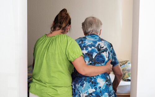 Eine Pflegerin stützt eine Seniorin beim Gehen.