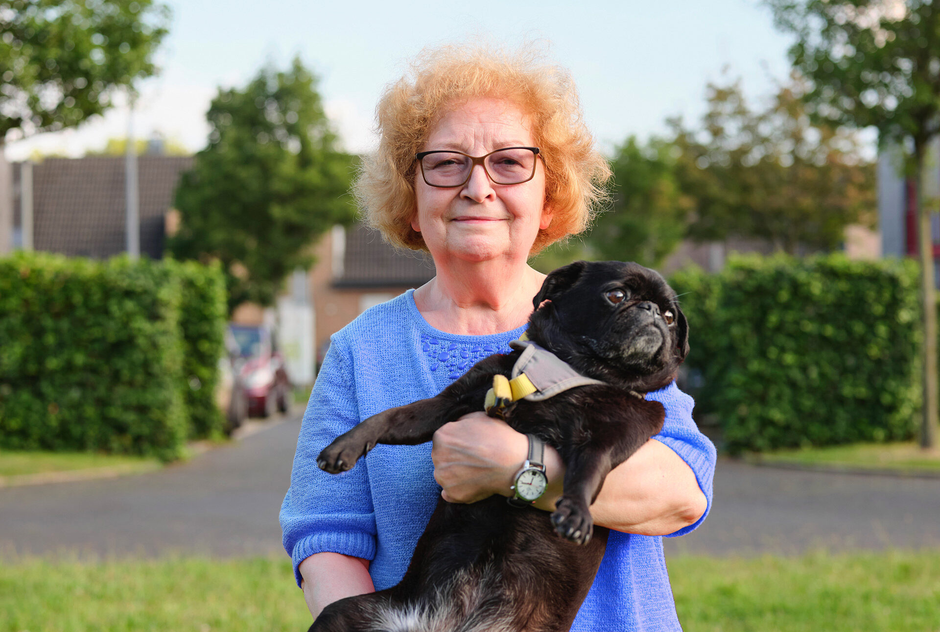 Eine Seniorin mit Brille trägt einen Hund auf dem Arm.