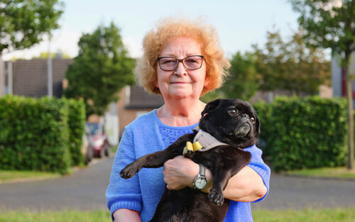 Eine Seniorin mit Brille trägt einen Hund auf dem Arm.