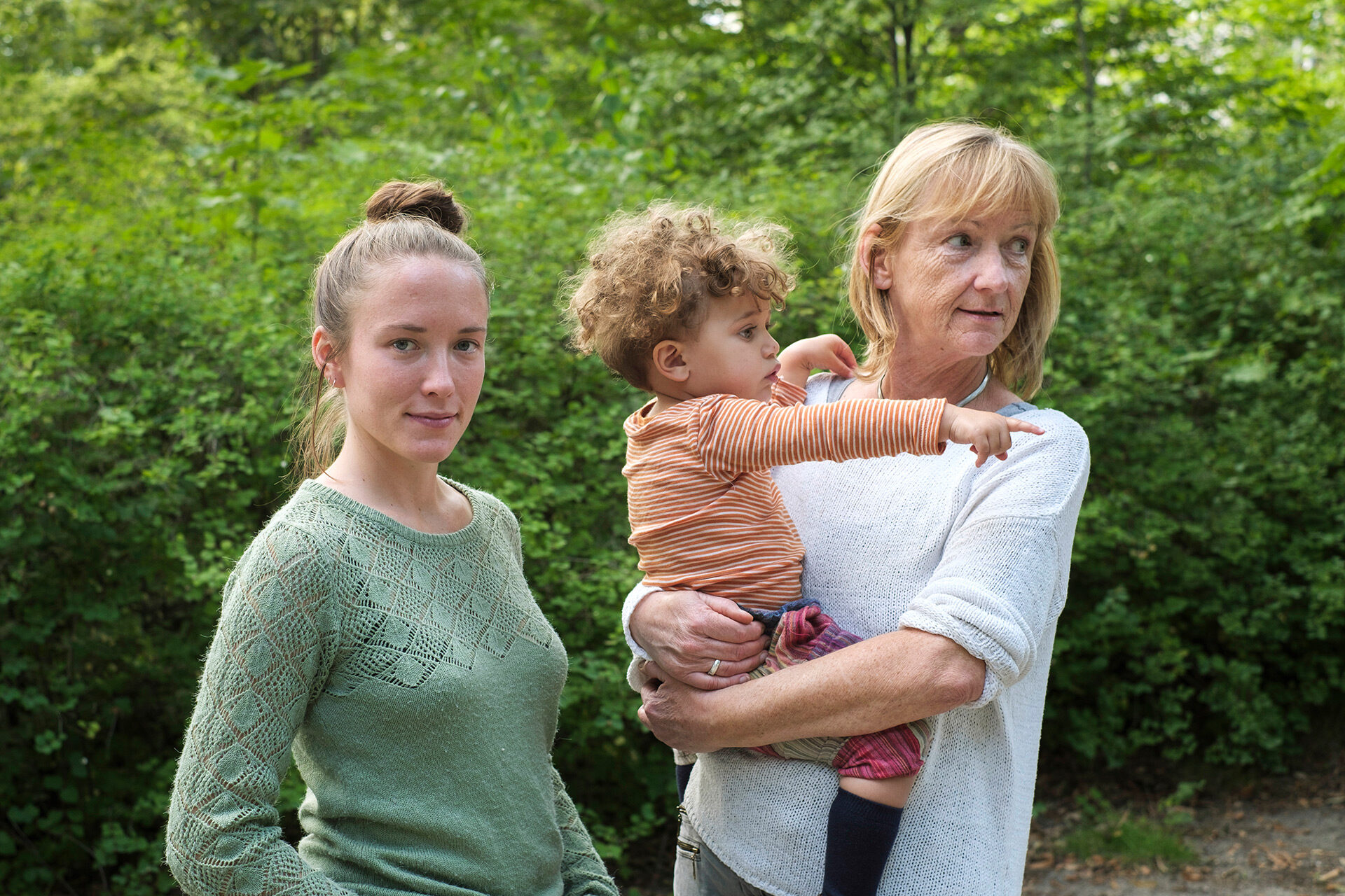 Eine junge Frau steht neben einer Seniorin mit kleinem Jungen auf dem Arm