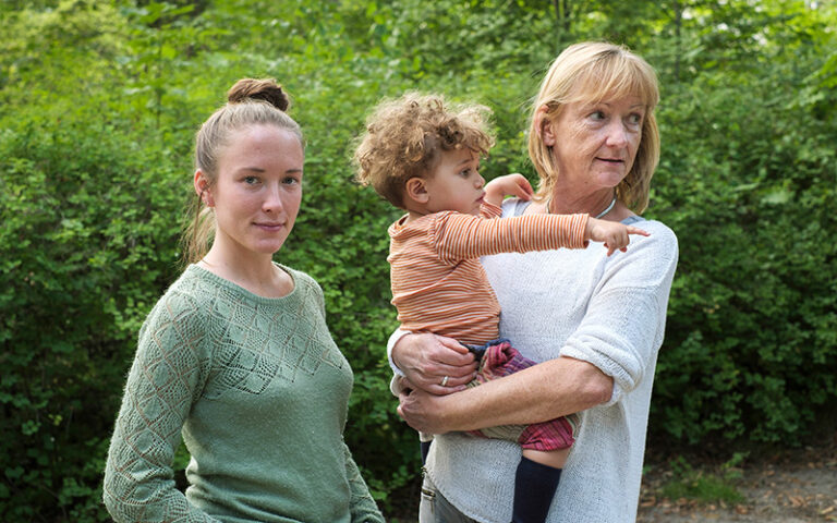 Eine junge Frau steht neben einer Seniorin mit kleinem Jungen auf dem Arm
