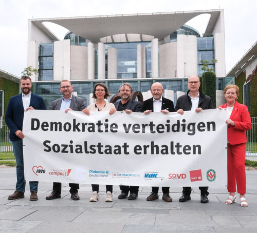 Vertreter*innen von ver.di, der AWO und weiteren Verbänden halten einen Banner "Demokratie verteidigen - Sozialstaat erhalten"