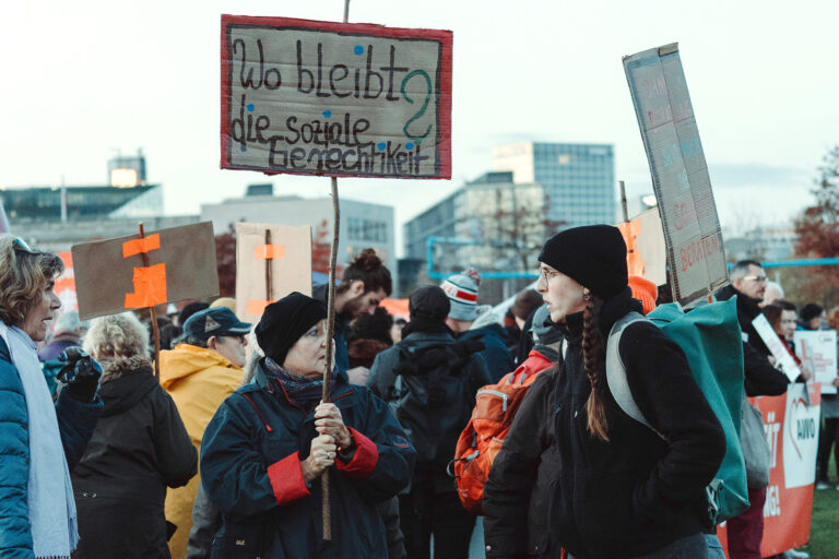Personen auf einer Demo, eine von ihnen hält ein Schild hoch "Wo bleibt die soziale Gerechtigkeit?"